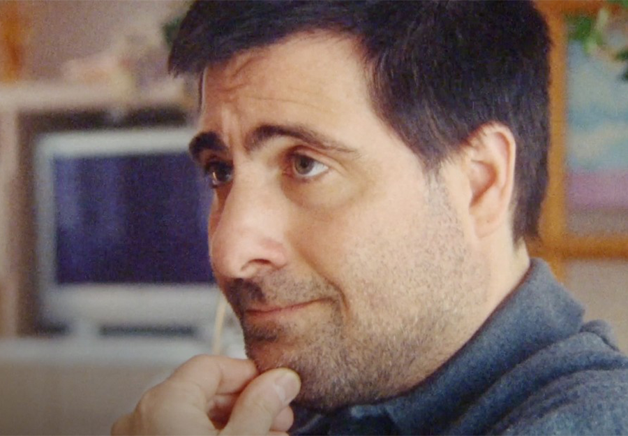 Man with black hair looking at someone with fingers on his chin.