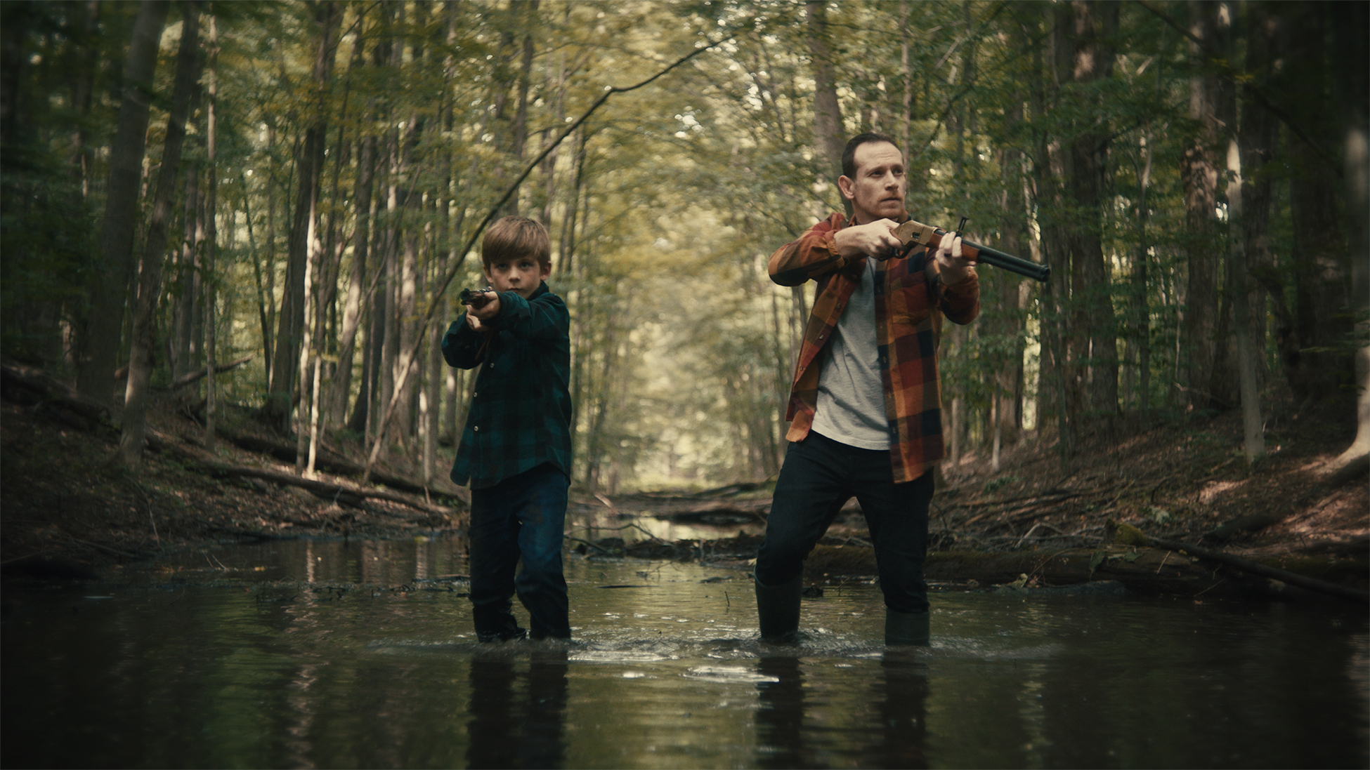 A father and son in the woods both holding guns.