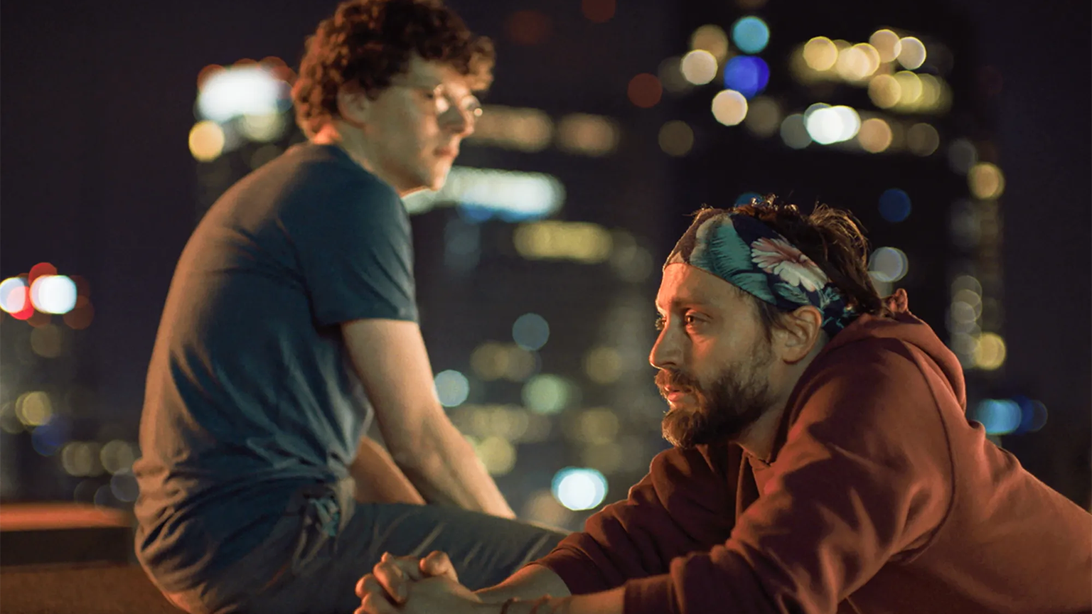 A man on a roof ledge with another next to him leaning.