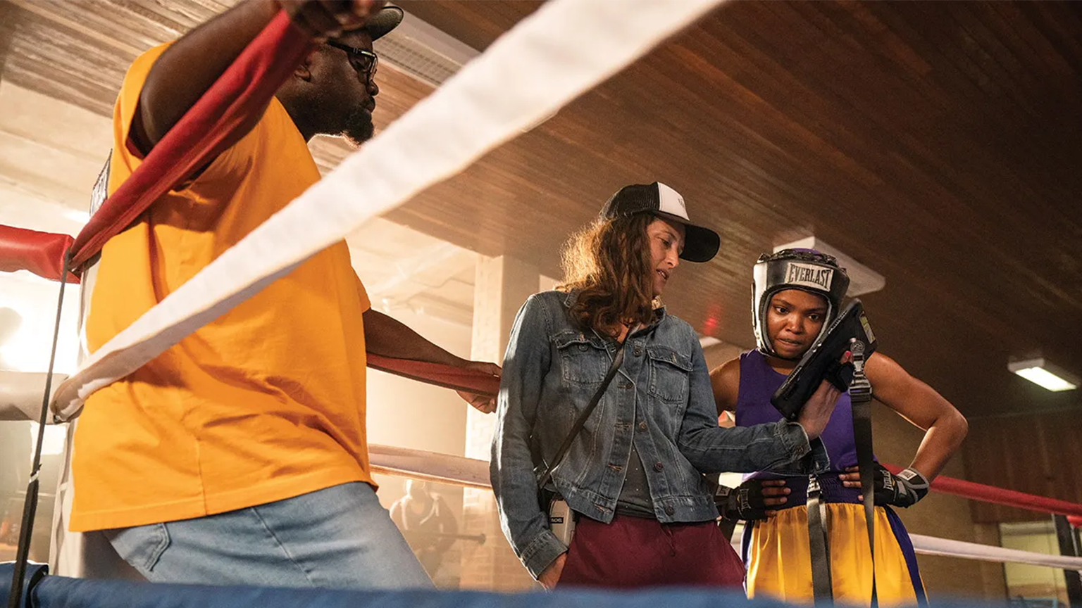 A female boxer looking at a woman's ipad in the ring with someone awaiting to fight her.