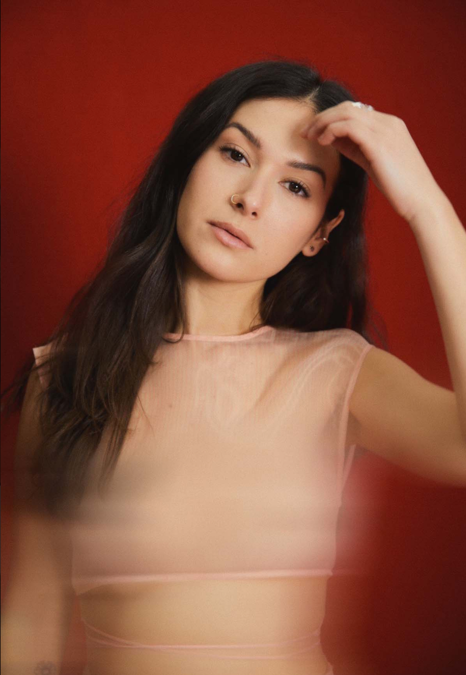 nella in black strap shirt with long brown hair down against a red background.