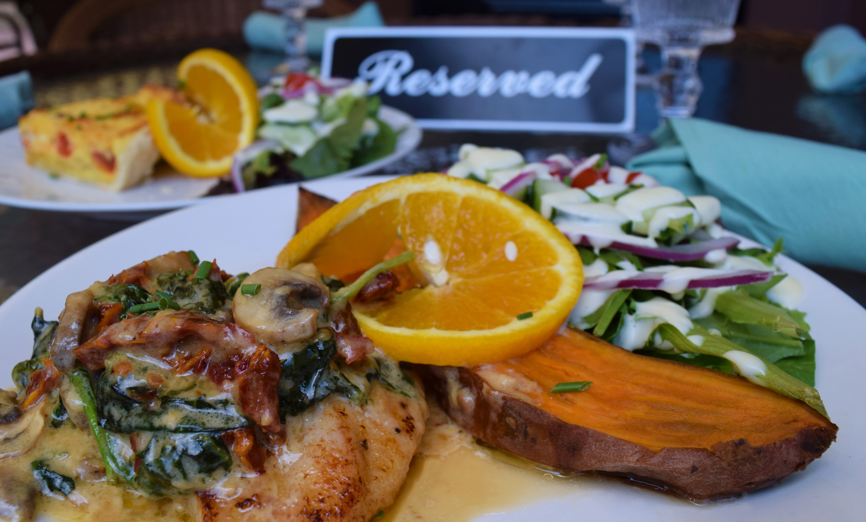 Chicken breast with mushrooms, sundered tomatoes next to a salad a roasted sweet potato