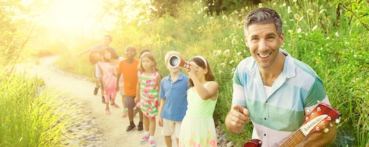 man with guitar being followed by a line of kids